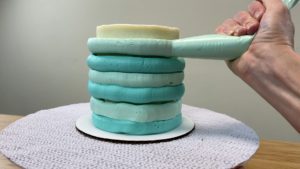 piping different colours of buttercream frosting stripes onto a cake