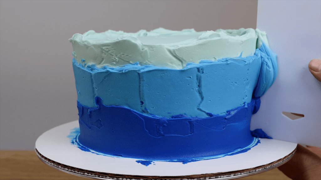 use cake scraper to take off excess frosting on the sides of the cake to start smoothing it Which Cake Scraper Is Best?