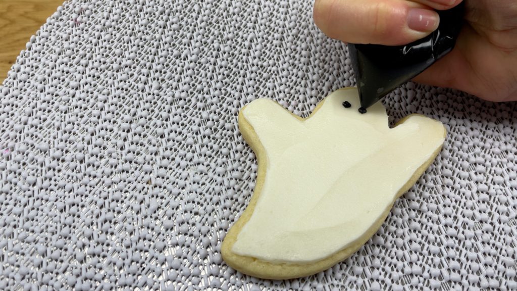 pipe faces onto ghost cookies with black buttercream 10 Halloween Cake Hacks