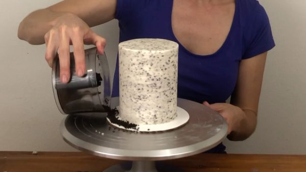 pour oreo cookie crumbs around cake board for cookies and cream cake