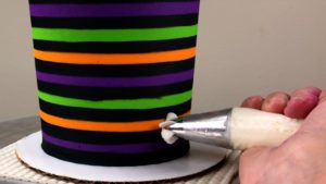 attach gold buttercream pumpkins to striped halloween cake with buttercream