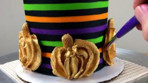 curve gold buttercream pumpkins against striped halloween cake using paintbrush