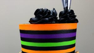 pipe black buttercream swirls on top of striped halloween cake with gold buttercream pumpkins