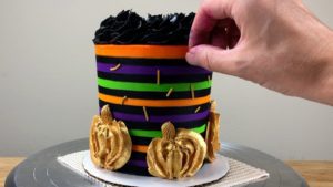 press gold sprinkles into Striped Halloween Cake With Gold Buttercream Pumpkins
