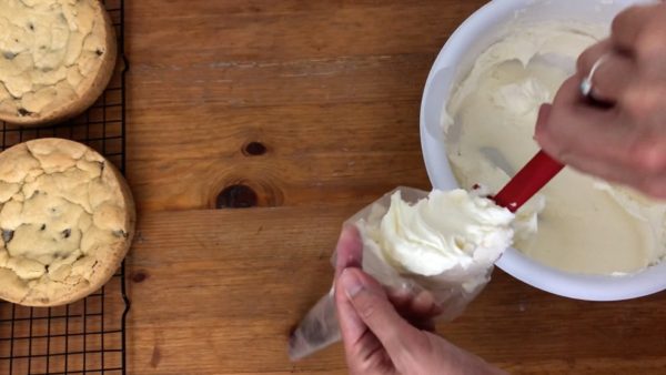 fill a piping bag with buttercream for filling of chocolate chip cookie cake