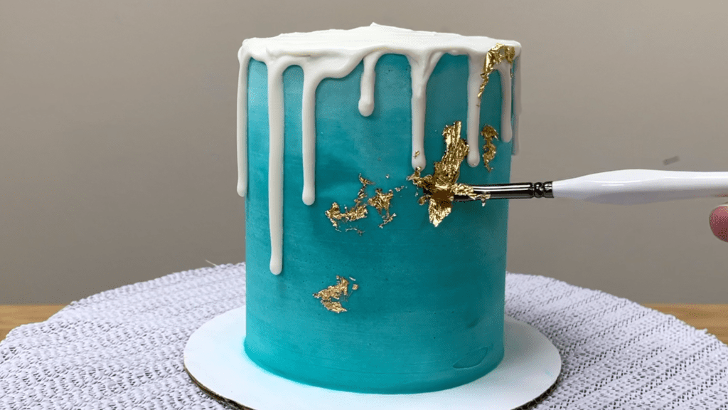 brush gold leaf onto frosting on cake How To Use Gold Leaf On Cakes