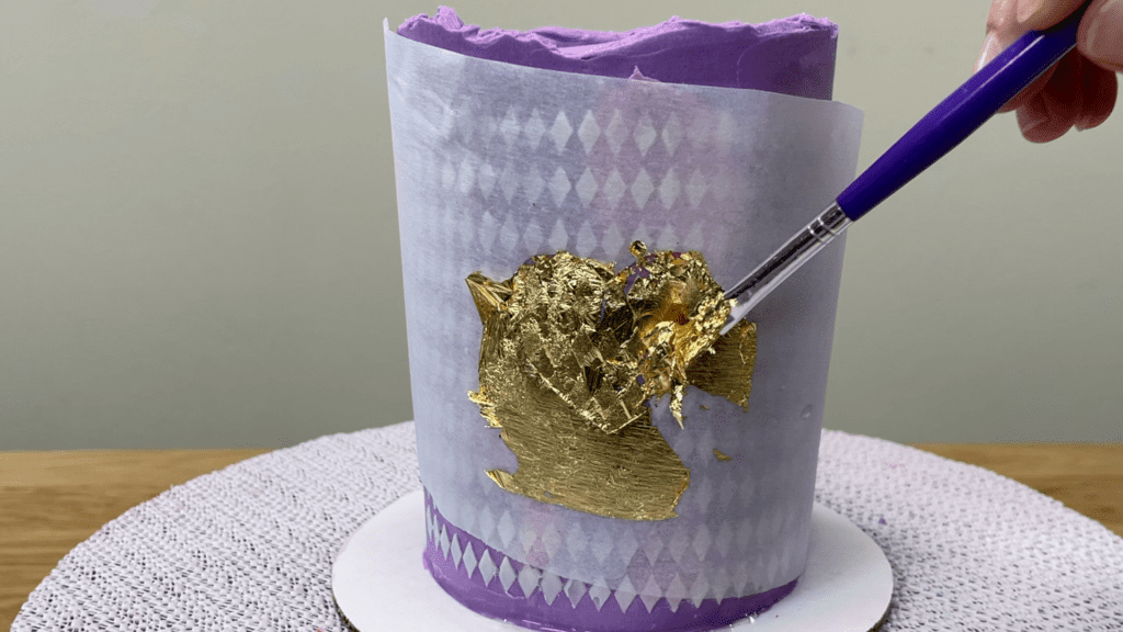 fill in gaps in stencil by brushing on more gold leaf before removing stencil How To Use Gold Leaf On Cakes