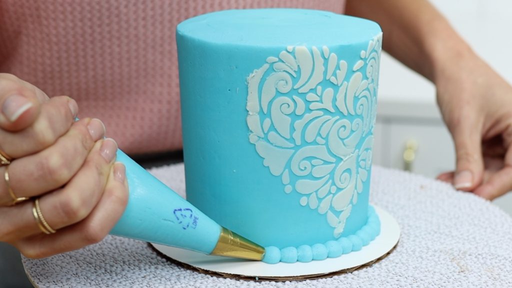 piping a beaded border around a cake with a round piping tip Save or Splurge Improve your Cake Decorating with these Tools!