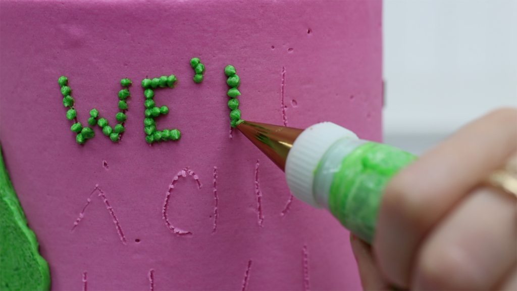 piping dots of buttercream onto a cake for pointillist writing a message