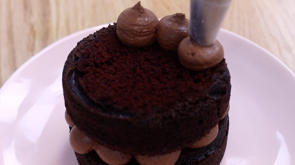 piping chocolate ganache filling onto a cake