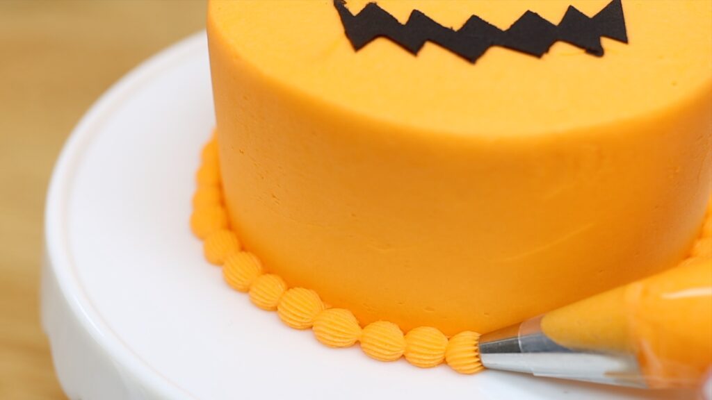 piping border onto mini cake jack o lantern