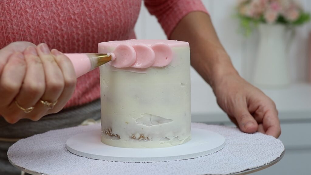 pipe dots of frosting in a row to make scalloped frosting on a cake