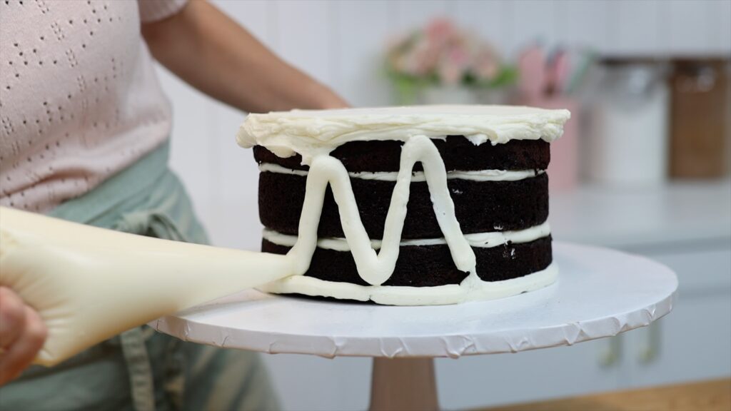 piping buttercream frosting onto semi naked tier cake