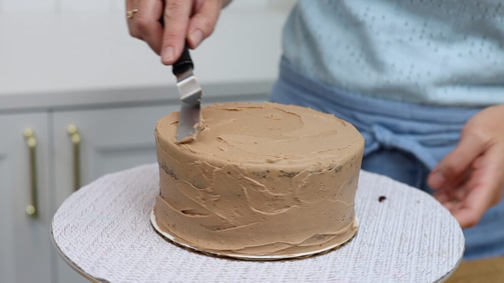 crumb coat frosting on cake on cake board the same size as the cake