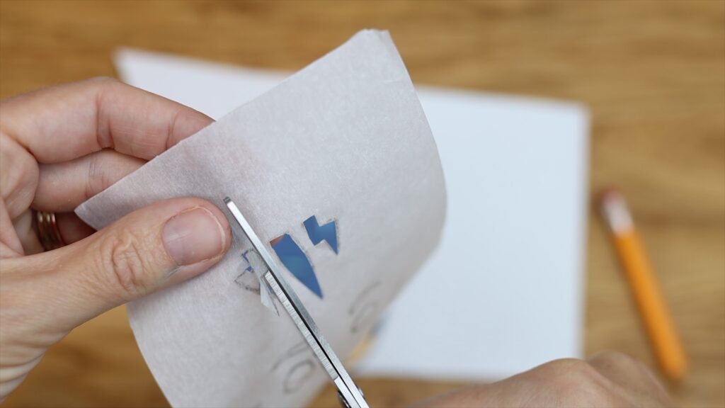 cut out details of character from parchment paper to make homemade stencils for cake