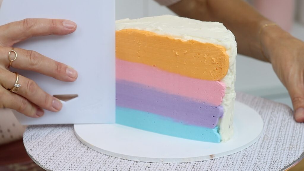 smoothing frosting on a rainbow half birthday cake