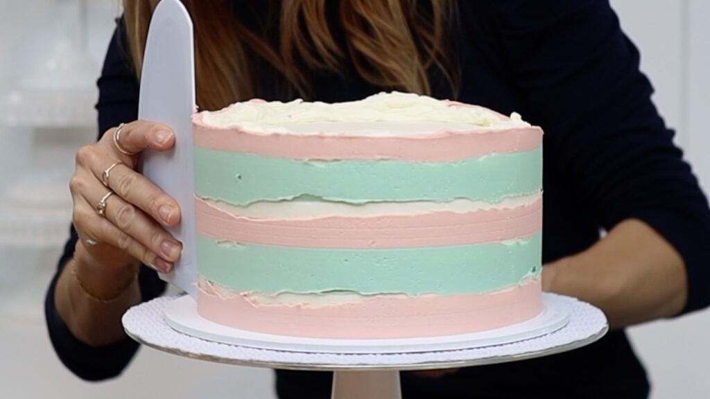 scraping buttercream stripes on a cake