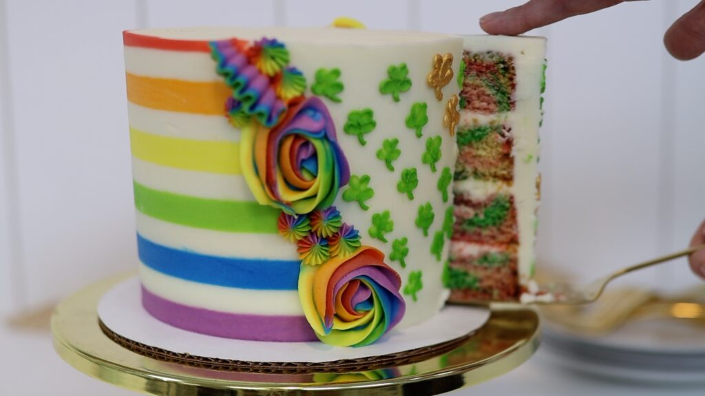 slicing and serving a buttercream rainbow stripe cake