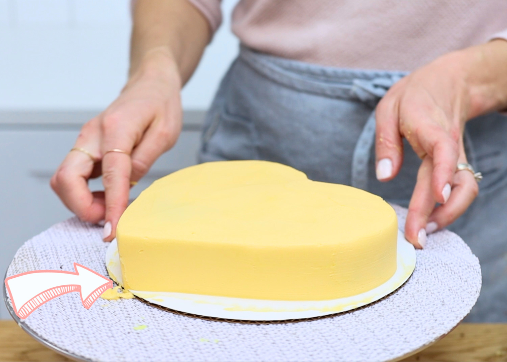 A cake sitting on a cake board that’s too small, with the frosting reaching right to the edge